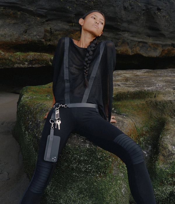women siting on a rock wearing V net top, moto leggings, leather belt phone case with metal key clip