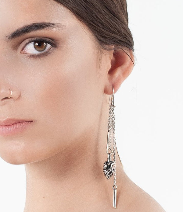 Close-up of a woman wearing a silver earring with a heart charm on a white background