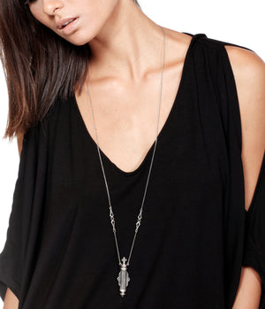 Person wearing a black top with a long necklace featuring a pendant.