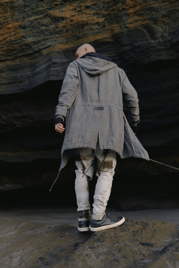 Unisex parka made of light weight linen. Featuring large lined hood, hidden snaps over front zip fastening, long sleeves with ribbed detail, snaps on cuffs, a drawstring waist, front frayed edge pockets, leather detail on cuffs, collar and back, leather tassel zip on outside chest pocket, earphone loop on inside chest pocket, a drawstring hem and a mid-length.