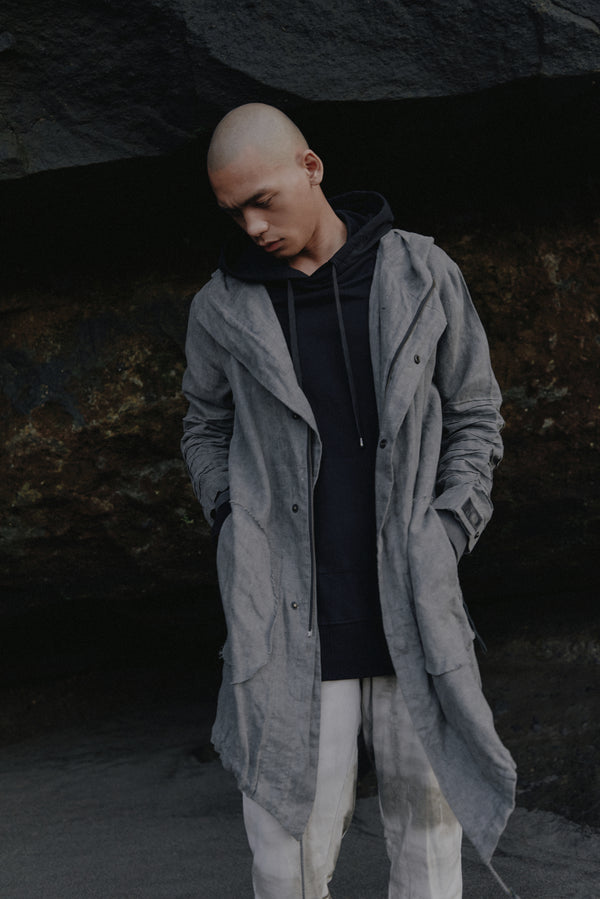 Unisex parka made of light weight linen. Featuring large lined hood, hidden snaps over front zip fastening, long sleeves with ribbed detail, snaps on cuffs, a drawstring waist, front frayed edge pockets, leather detail on cuffs, collar and back, leather tassel zip on outside chest pocket, earphone loop on inside chest pocket, a drawstring hem and a mid-length.