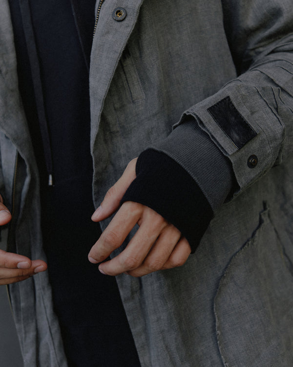 Unisex parka made of light weight linen. Featuring large lined hood, hidden snaps over front zip fastening, long sleeves with ribbed detail, snaps on cuffs, a drawstring waist, front frayed edge pockets, leather detail on cuffs, collar and back, leather tassel zip on outside chest pocket, earphone loop on inside chest pocket, a drawstring hem and a mid-length.